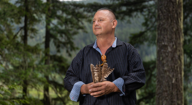 Chief James Hobart holding spotted owl feathers in front of a forest backdrop
