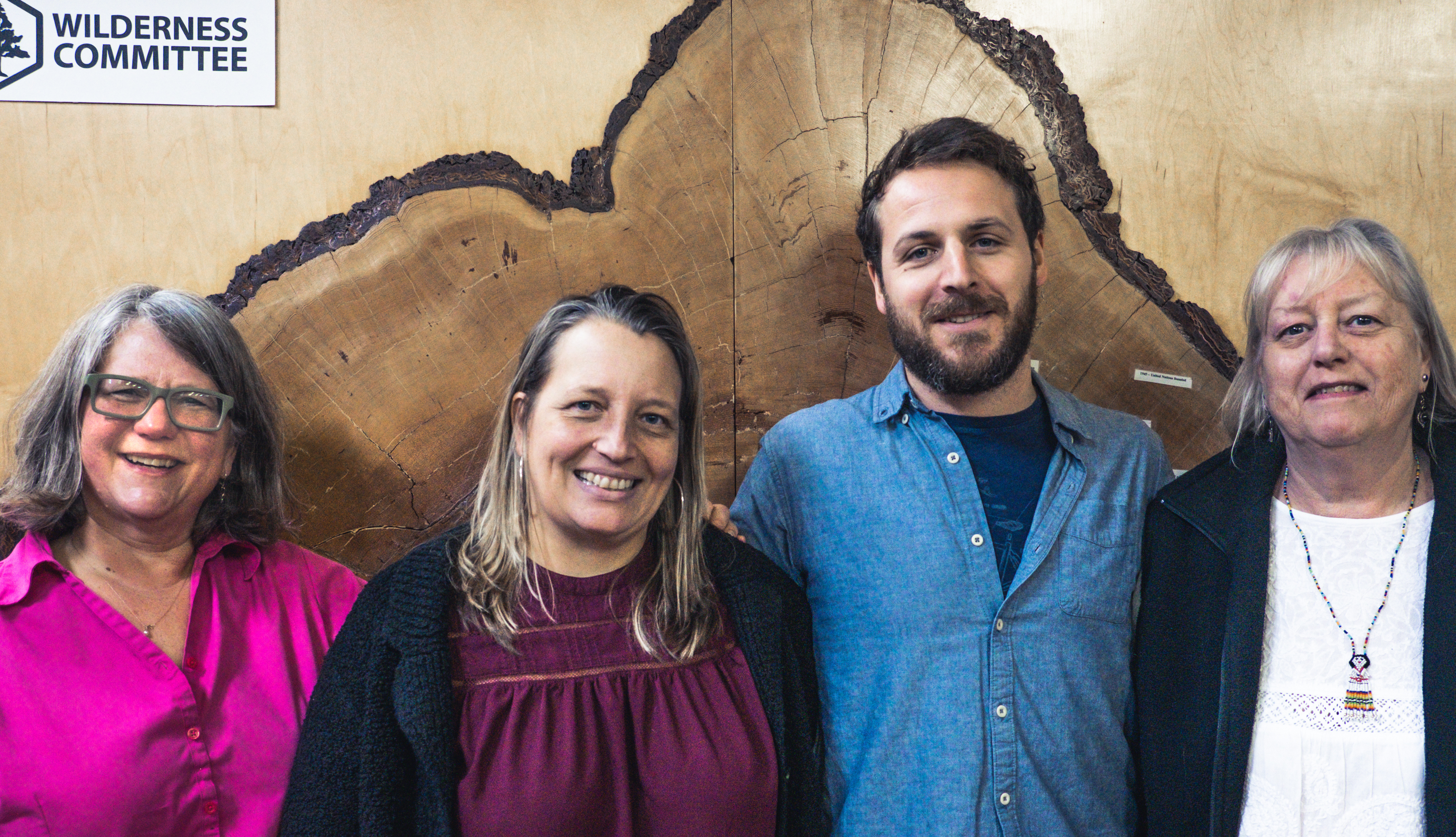 Four people standing together in front of a big tree cross section.