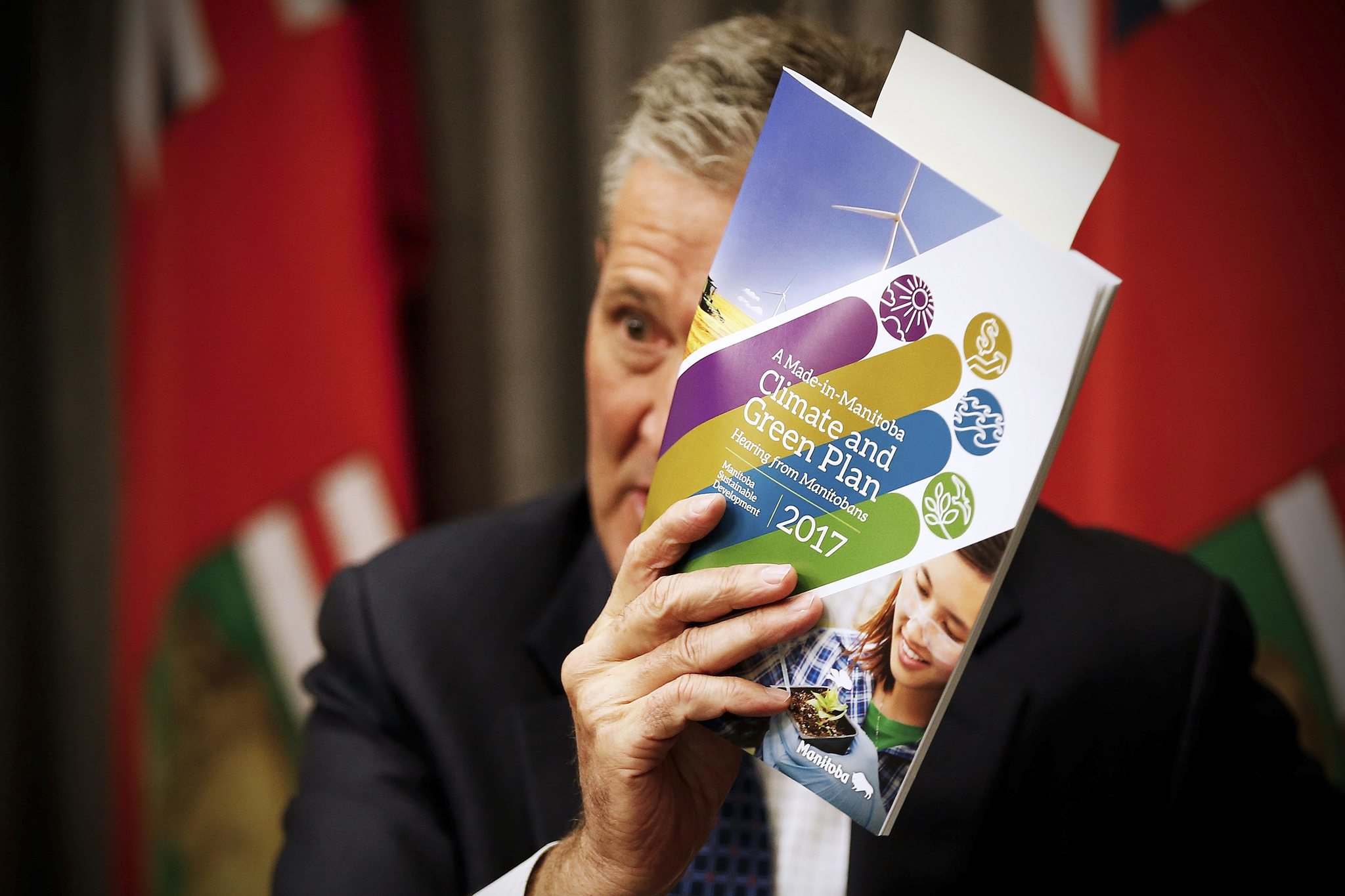 Premier Brian Pallister holding up a copy of the 2017 Manitoba Climate and Green plan.