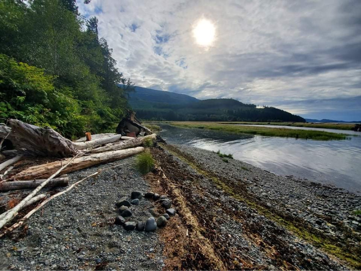 Hiladi village site, Ma’amtagila territory. A photo of a rocky beach with forests on one side, and the sea on the other. End of image description. 