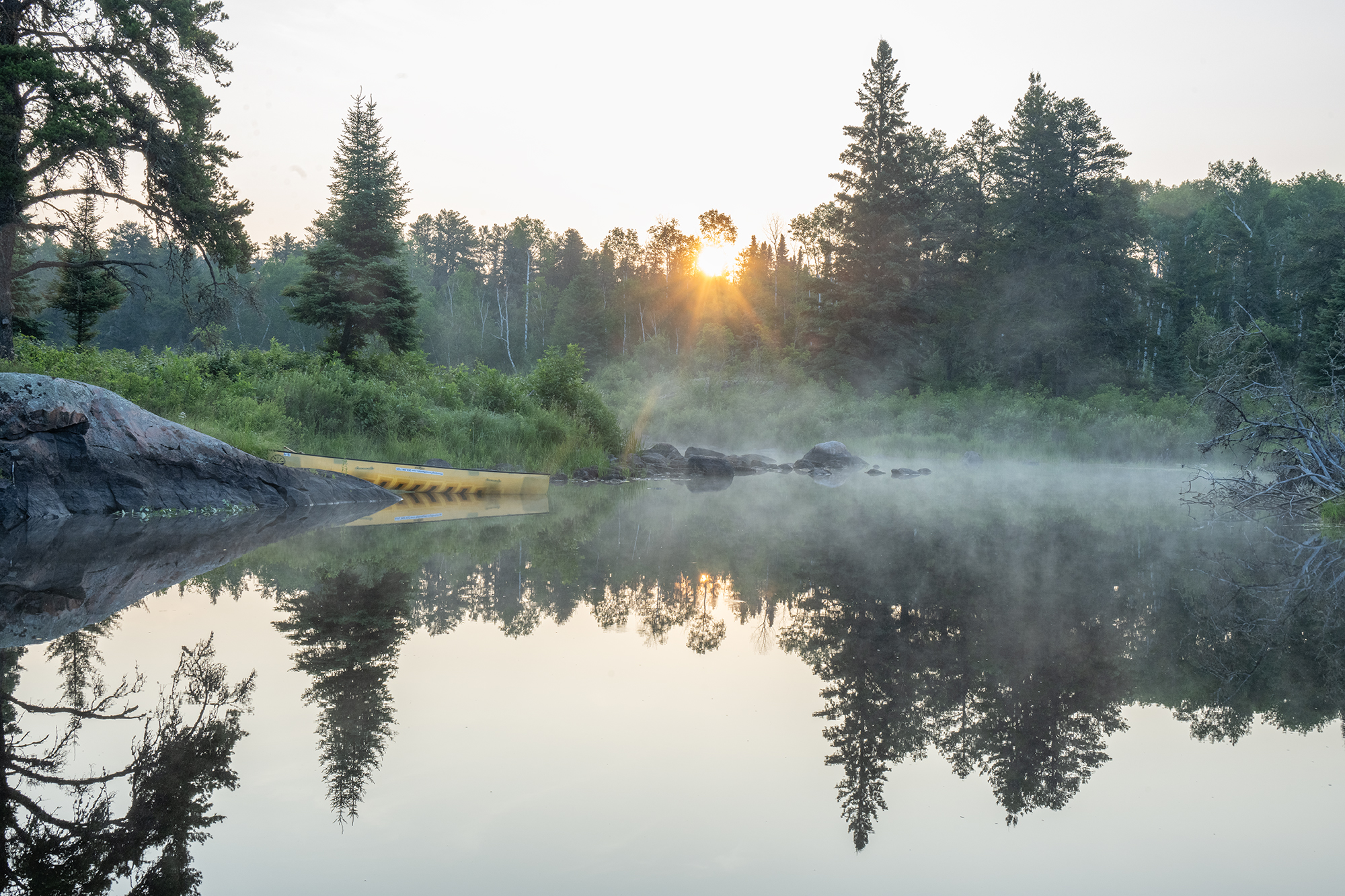 A yellow canoe sits on the lower Bird River during a foggy sunrise