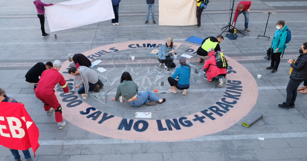 A group of people drawing a sign on the ground that says "110,000 people says no LNG + Fracking". End of image description.