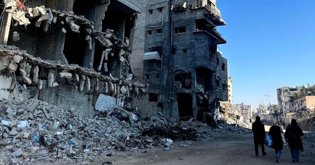 A bombed building in shambles in Gaza. Three people are walking away.