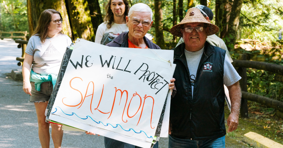 Two people holding up a sign that says "we will protect the salmon"