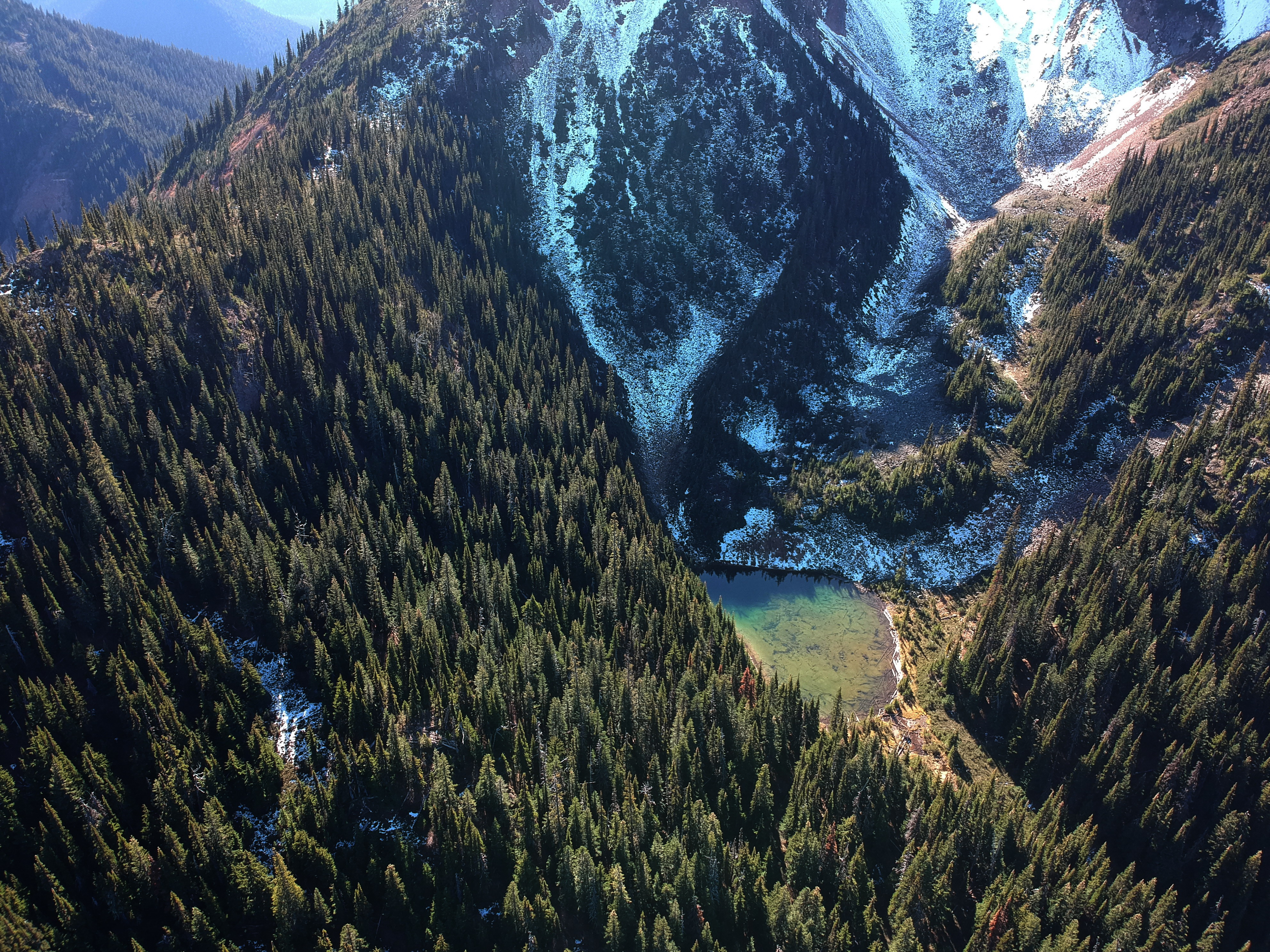 An aerial shot of the Donut Hole, a small valley cut into thick forest and shadowed between two mountain peaks.