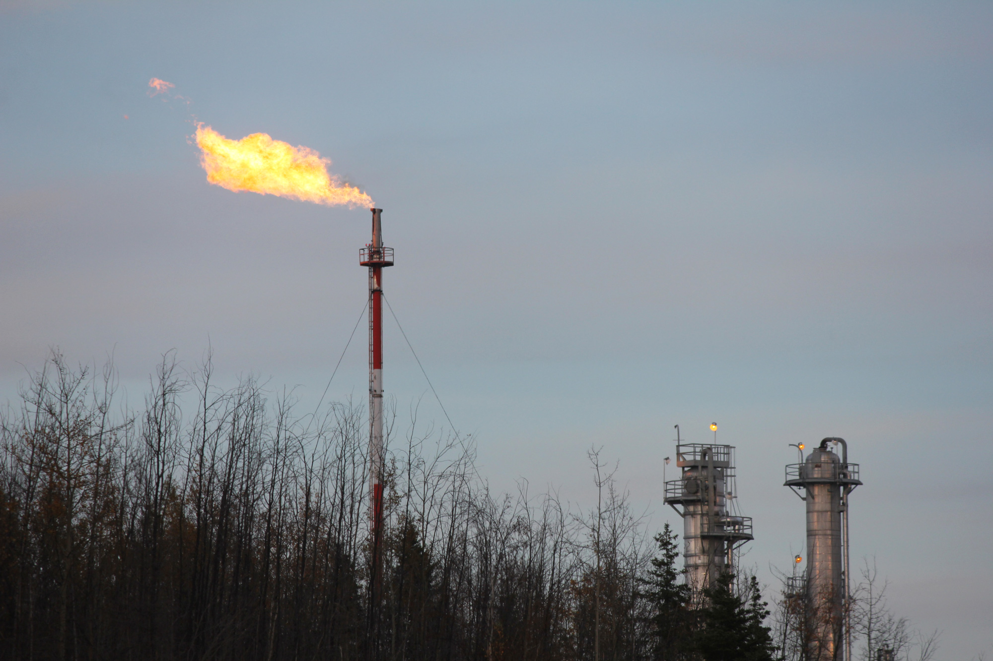 A flarestack at a fracking facility against an evening sky.