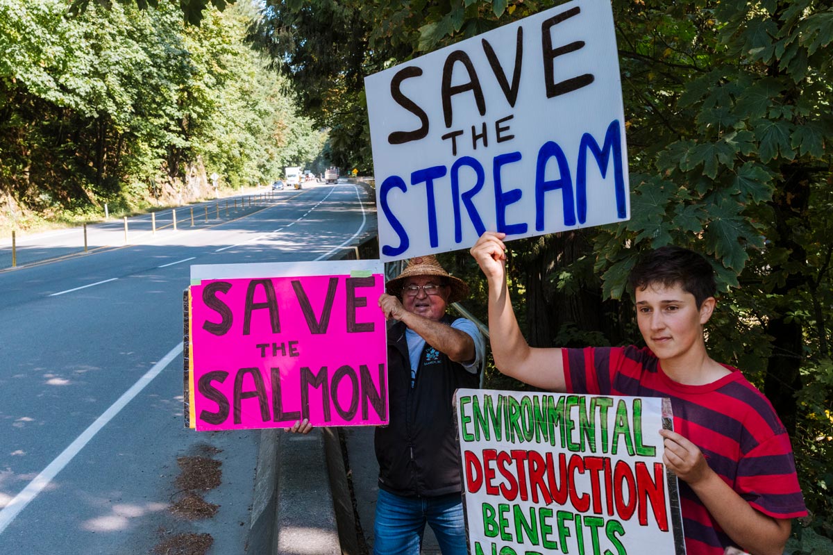 Campaigner Tobyn and Elder ZȺWIZUT Carl Olsen protesting with painted signs along the Malahat highway.