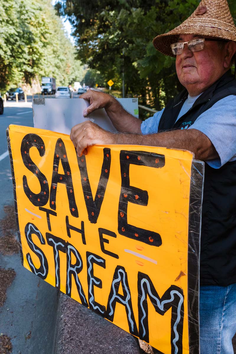 WSÁNEĆ Elder Carl Olsen with a yellow sign that reads "Save The Stream"