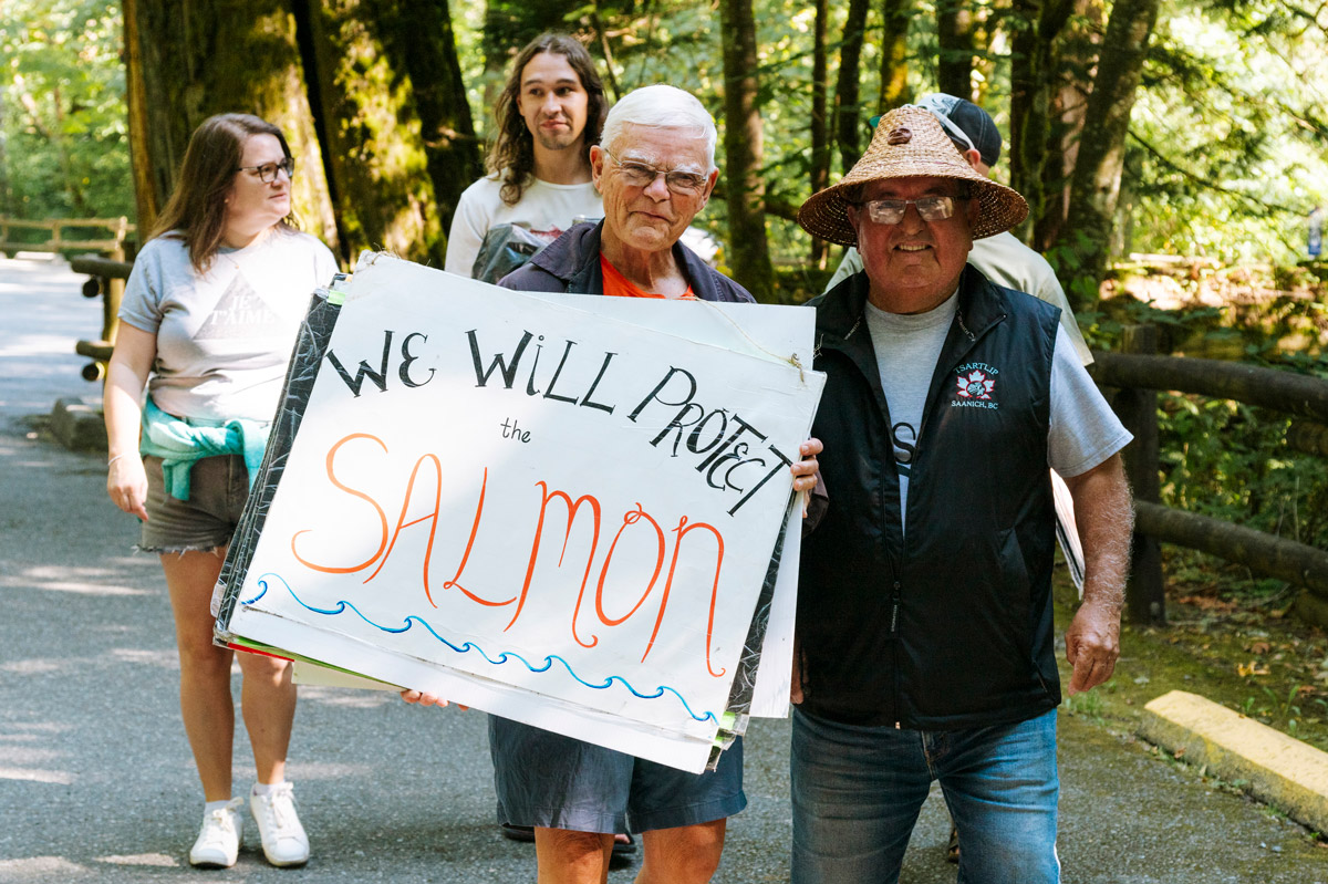 A small group of people stand around a home-made sign reading "We Will Protect the salmon" 