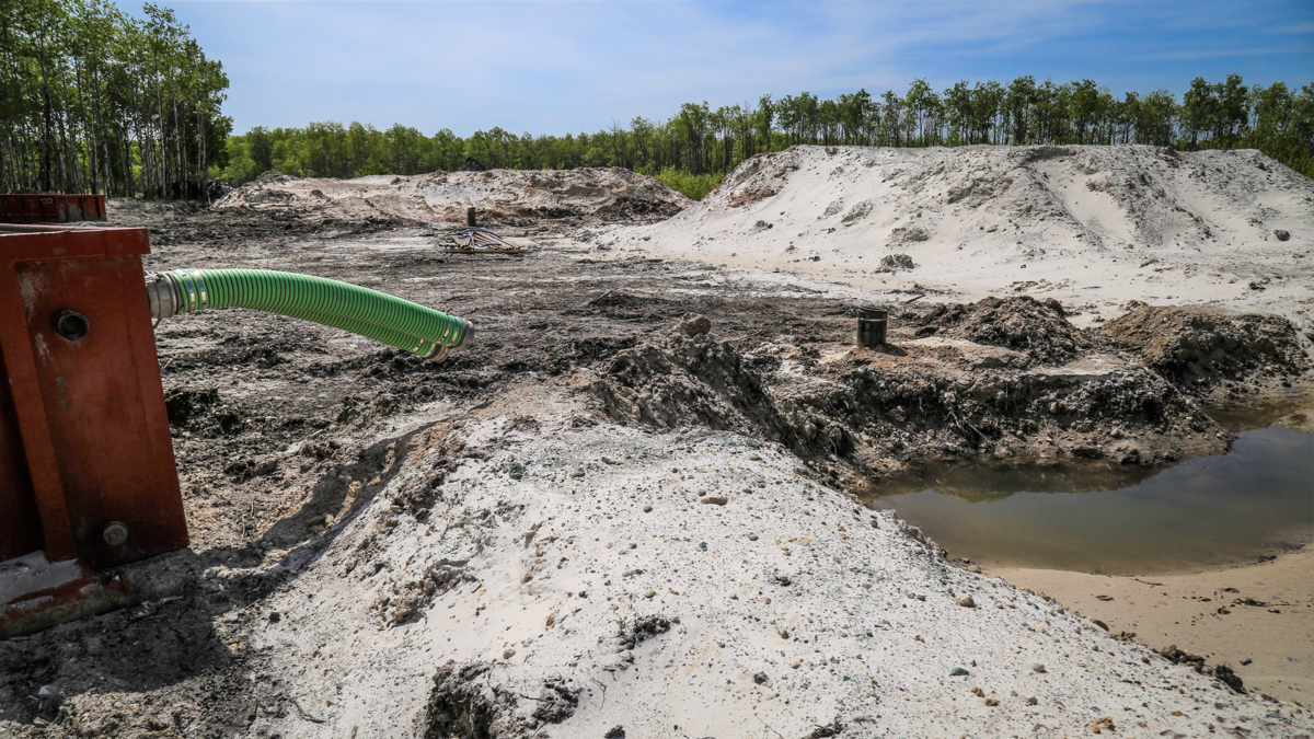 A wet pit of sand next to large orange pumps in a sand mine.