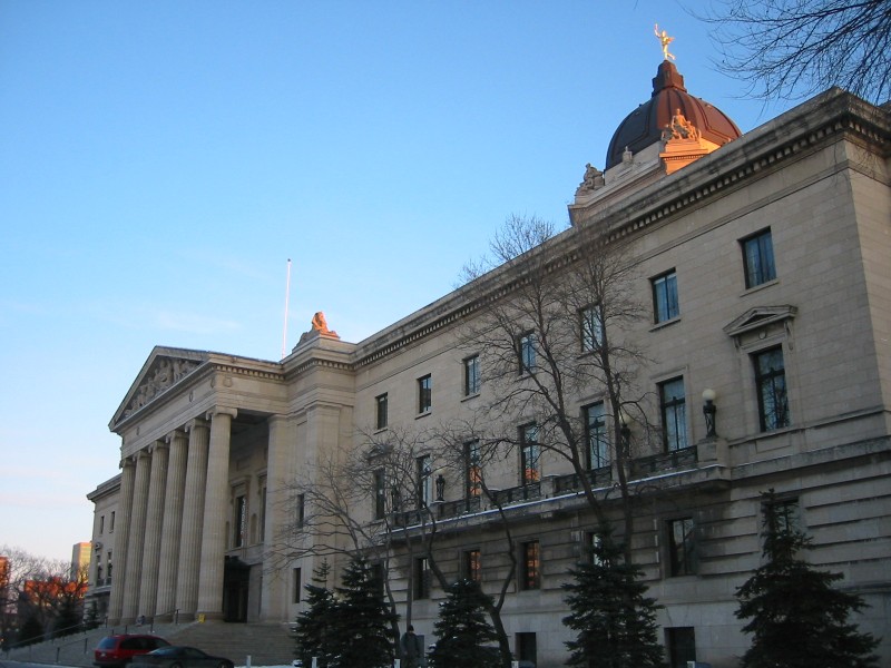 The Manitoba legislature. The imposing tan stone building is pictured at a steep angle, with the golden boy statue on top highlighted by the sun's rays.