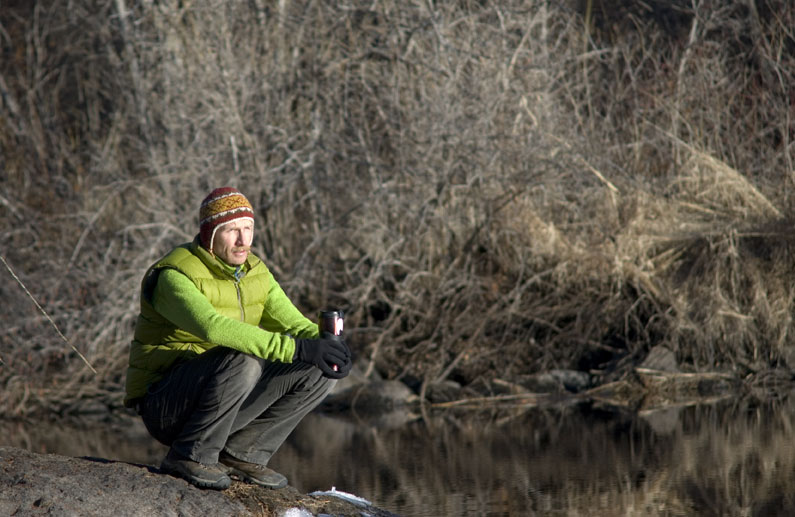 Eric crouching in the wilderness, staring at water.