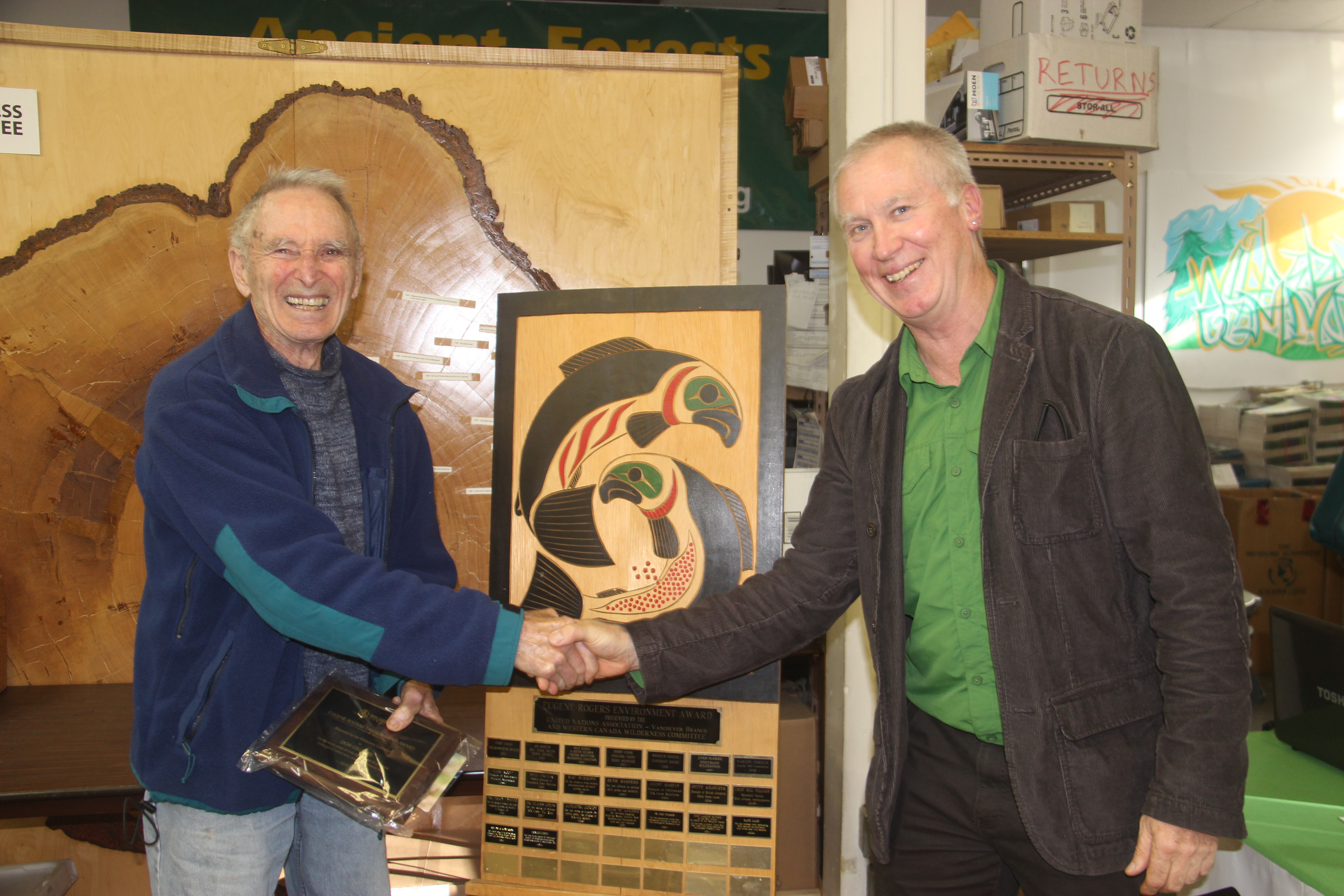 Joe Foy and Don Gillespie shaking hands in front of the Eugene Rogers award plaque at the Wilderness Committee head offce