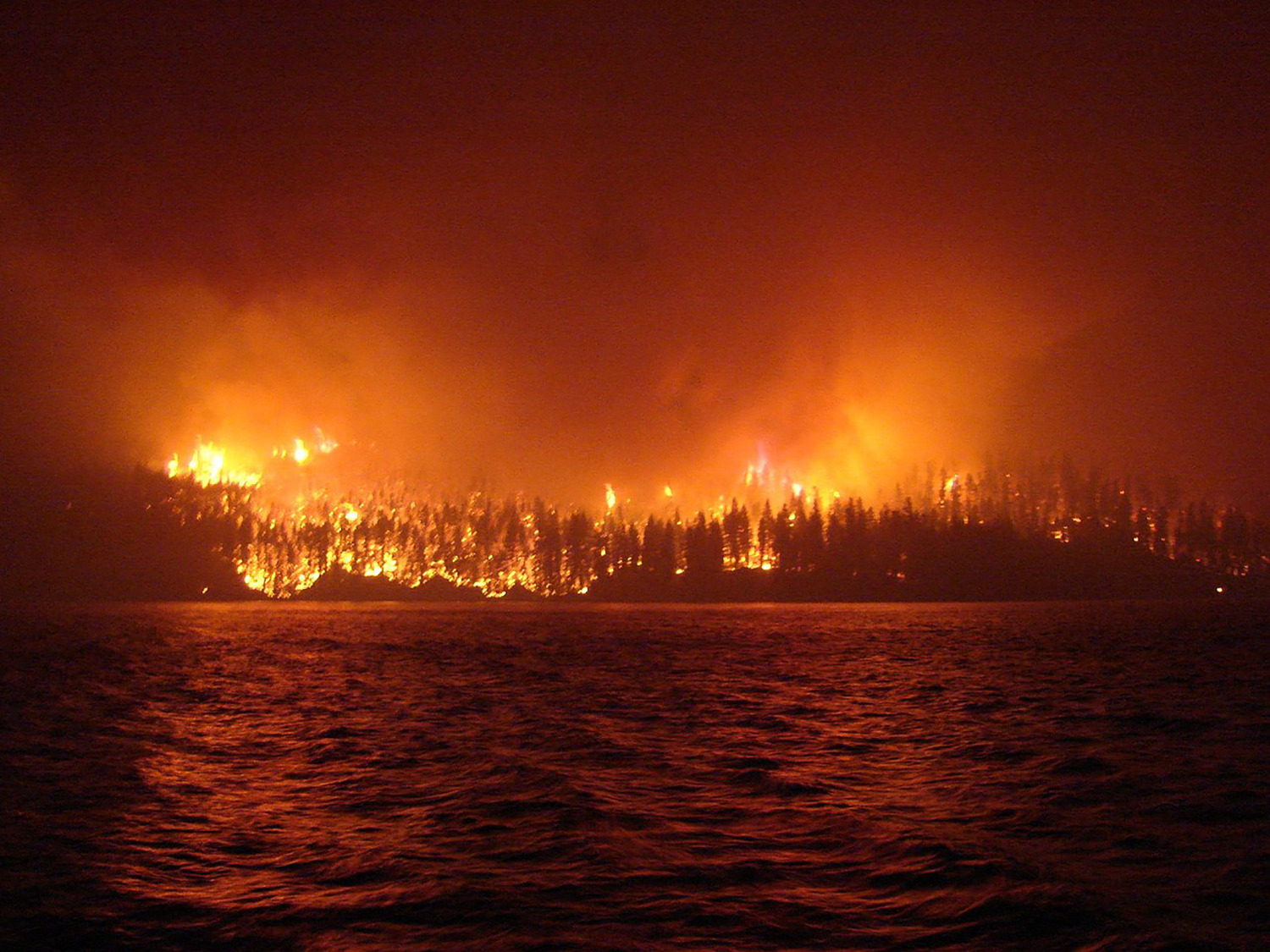 Forest on fire across the river. End of image description.