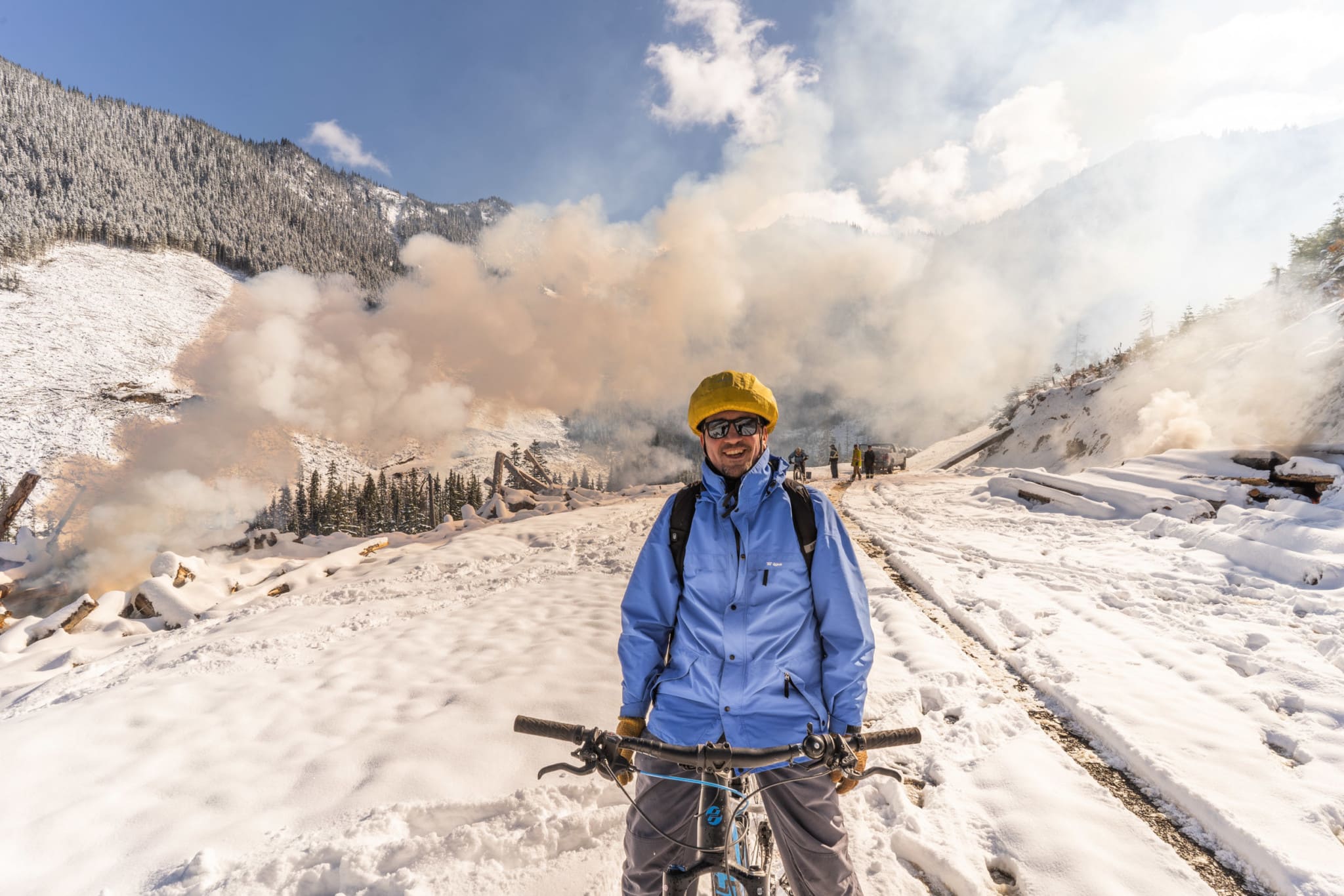 Author Chris Pollon rides an electric bike in the Manning Park ‘Doughnut Hole.’ Slash piles from recent clearcut logging on East Point Mountain are being burned by forestry company contractors, sending great plumes of smoke into the sky. Photo: Fernando Lessa / The Narwhal