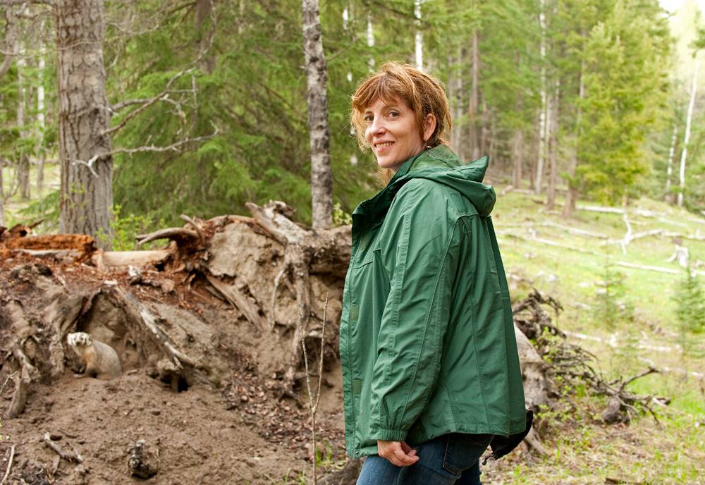 Gwen Barlee smiling over her shoulder in front of a badger den with endangered American badger