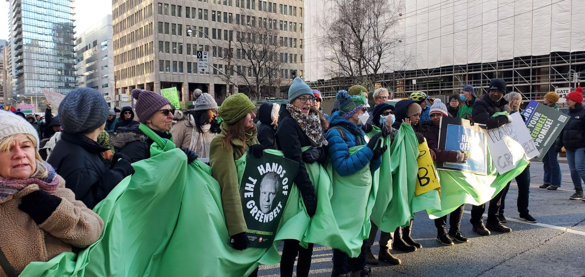 A group of people lined up holding up a banner about the greenbelt. End of image description.