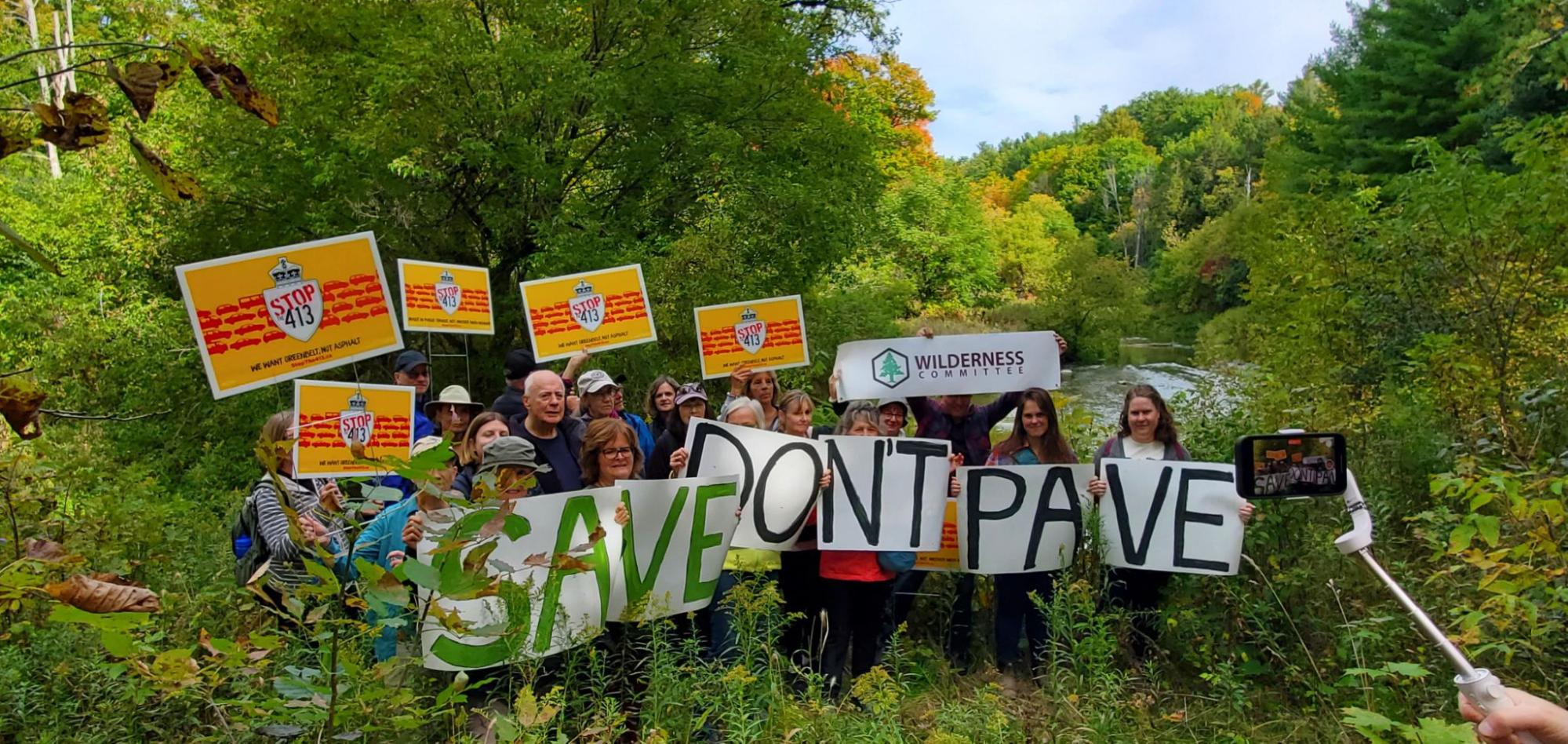 A group of people in the Greenbelt with a banner that says "Save don't pave". End of image description. 
