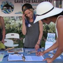 Someone signing up for action alerts at a Wilderness Committee event table with two volunteers