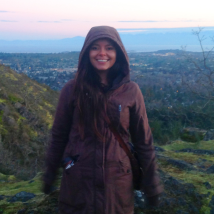 A person standing on mountains, wearing a jacket and smiling at the camera. End of image description.