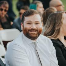 A male presenting person with a beard smiling at the camera. End of image description.