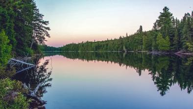 A glassy lake at sunset with forested shores