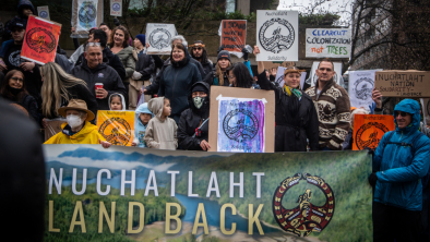 A group of people holding up various signs and banners expressing support for the Nuchatlaht Nation. End of image description. 