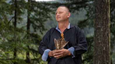 Chief James Hobart holding spotted owl feathers in front of a forest backdrop