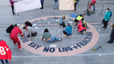 A group of people drawing a sign on the ground that says "110,000 people says no LNG + Fracking". End of image description.