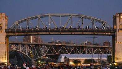 A call to stop PRGTCA in lights shine on a bridge against a dusky summer evening sky
