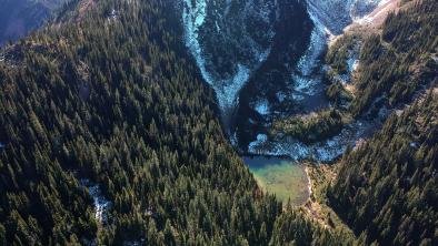 An aerial shot of the Donut Hole, a small valley cut into thick forest and shadowed between two mountain peaks.