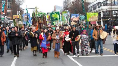 A group of people marching down a street. Some people are holding drums and others are holding banners.