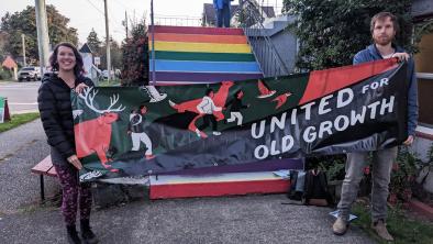 Two people holding a United for Old Growth banner outside an All Candidates Meeting.