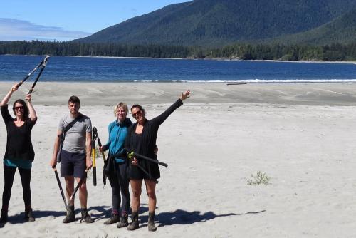 People stand on a big sandy beach in Clayoquot sound, holding clippers and backpacks for trail building