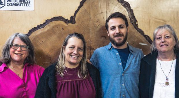 Four people standing together in front of a big tree cross section.