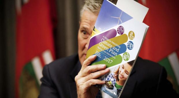 Premier Brian Pallister holding up a copy of the 2017 Manitoba Climate and Green plan.