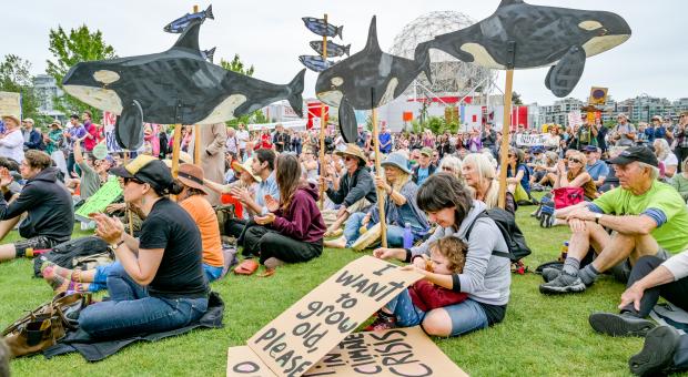 People sit on a grassy area with art and signs during a climate justice rally.