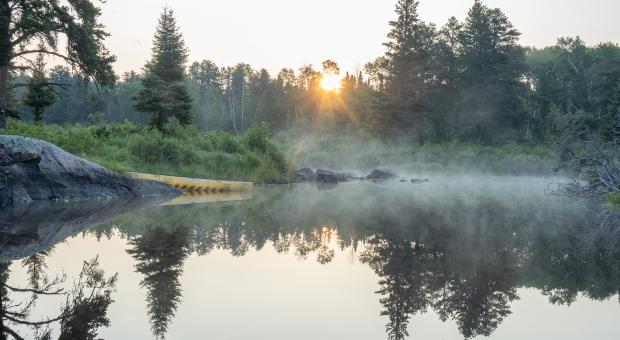 A yellow canoe sits on the lower Bird River during a foggy sunrise