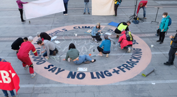 A group of people drawing a sign on the ground that says "110,000 people says no LNG + Fracking". End of image description.