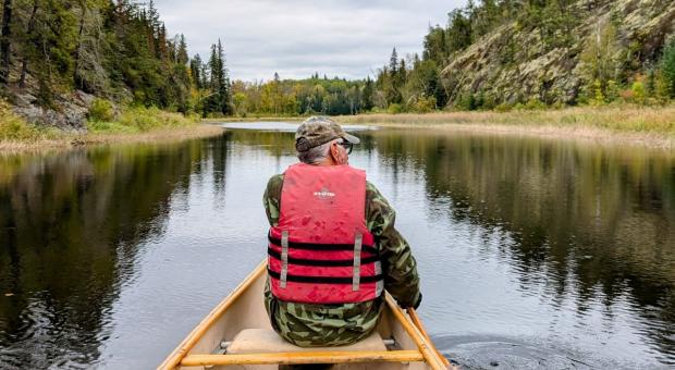 A man in a canoe on a river surrounded by forests. end of image description.