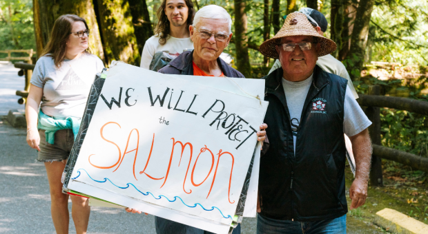Two people holding up a sign that says "we will protect the salmon"