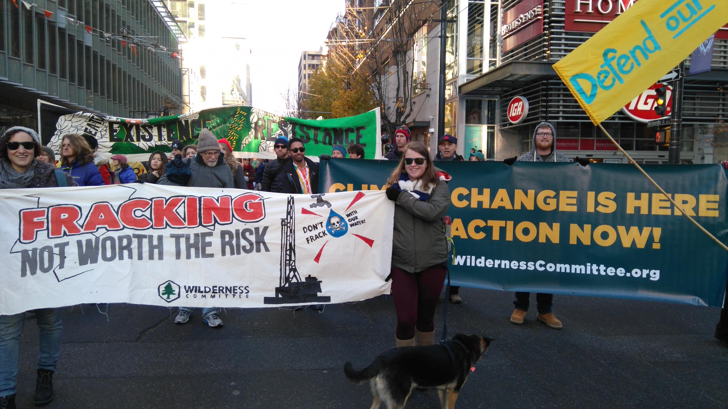 People hold banners that say "Fracking not worth the risk" and "Climate change is here, take action now!" during a march