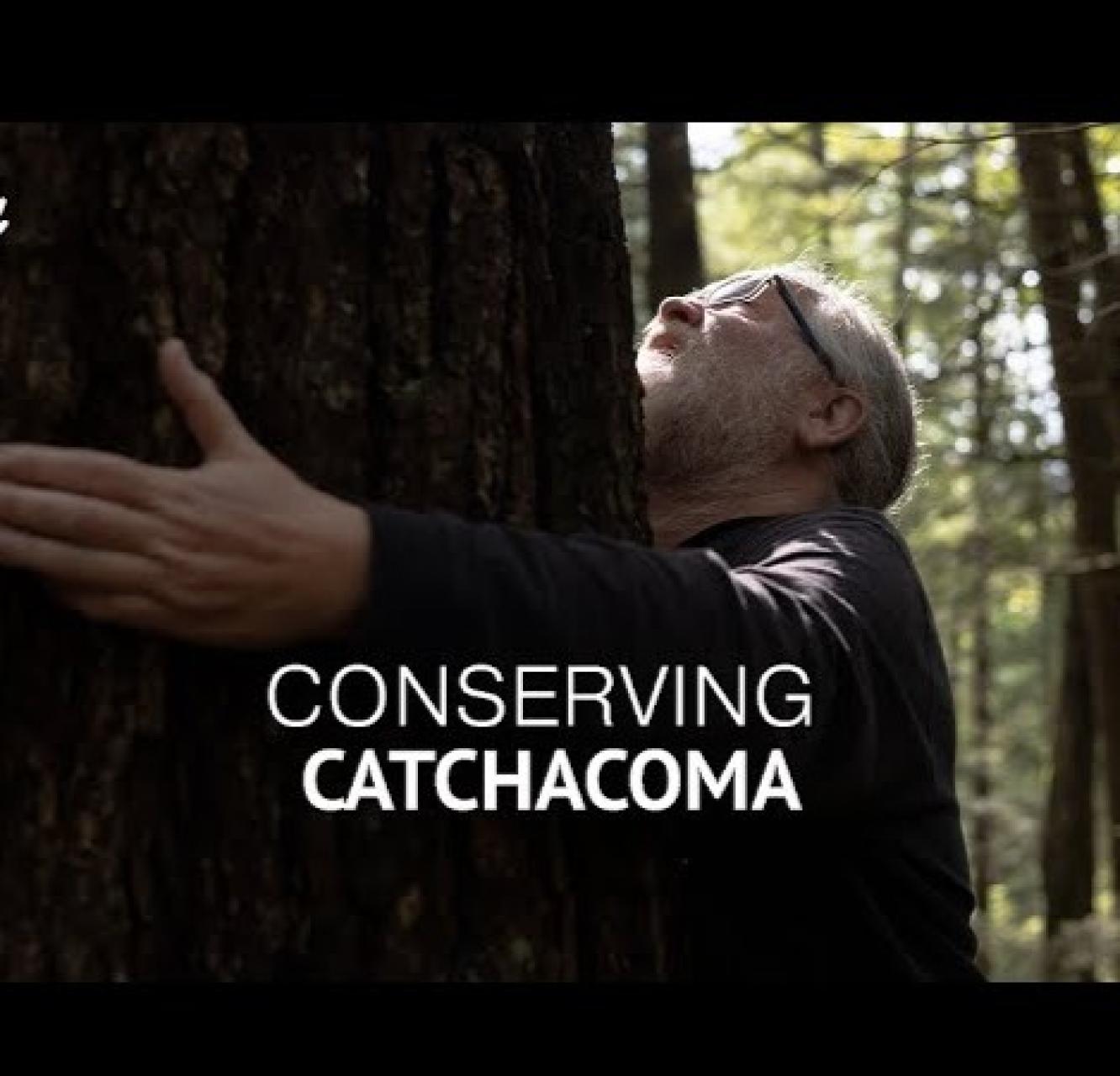 "Conserving Catchacoma" An older man with a light grey beard and hair hugs a huge tree.