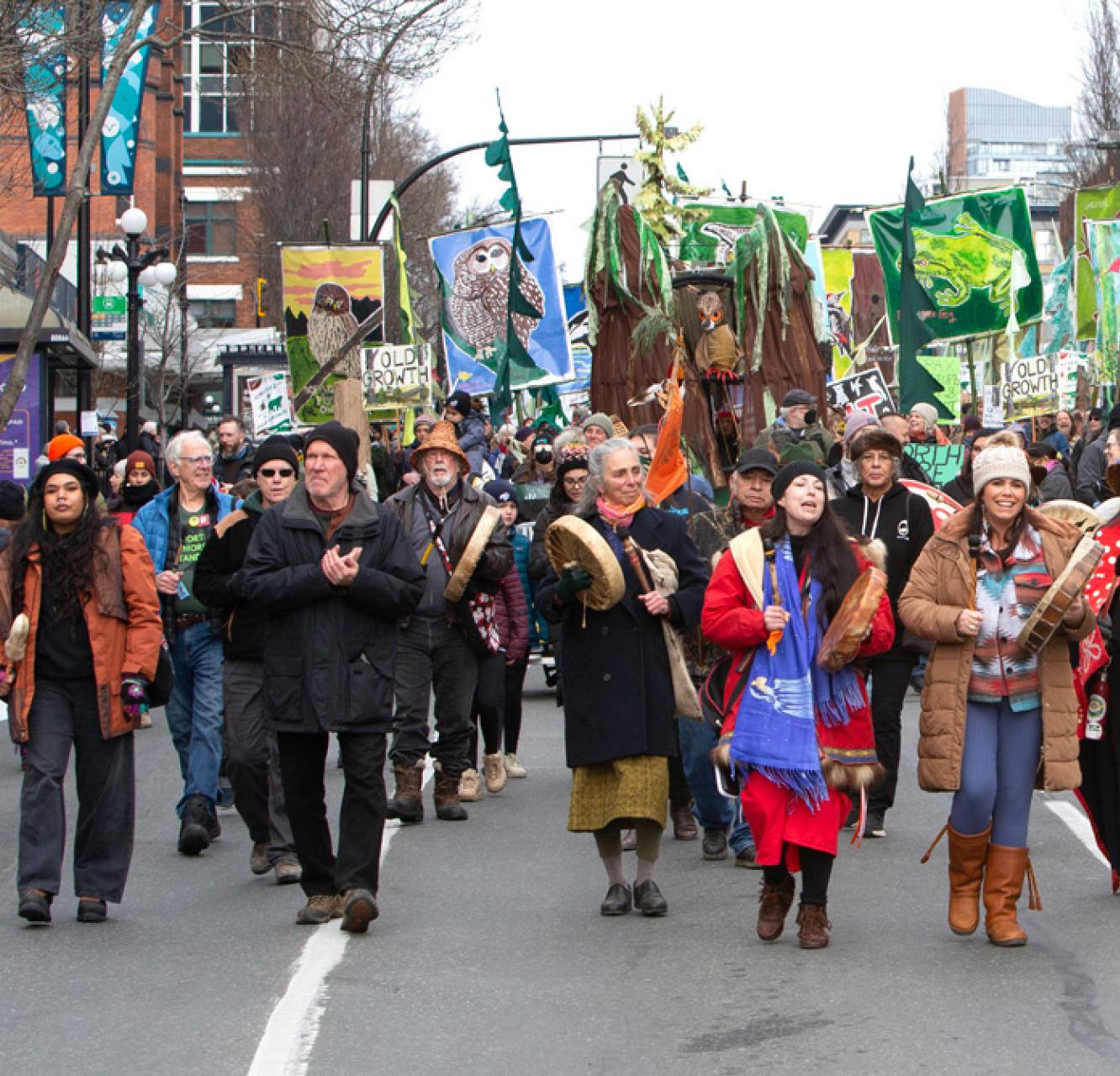 A group of people marching down a street. Some people are holding drums and others are holding banners.