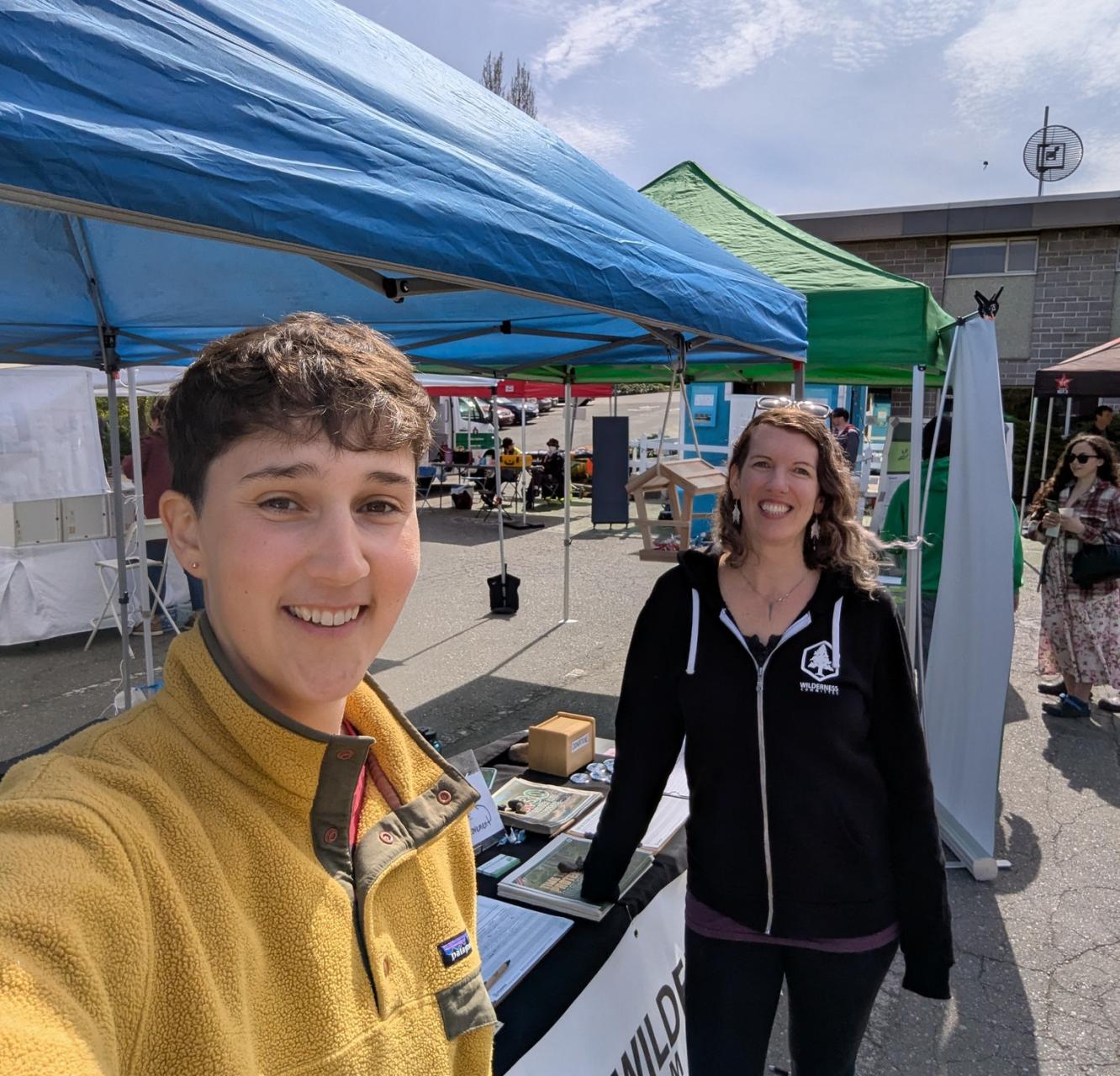 Two smiling people stand in front of a blue tent at a rally
