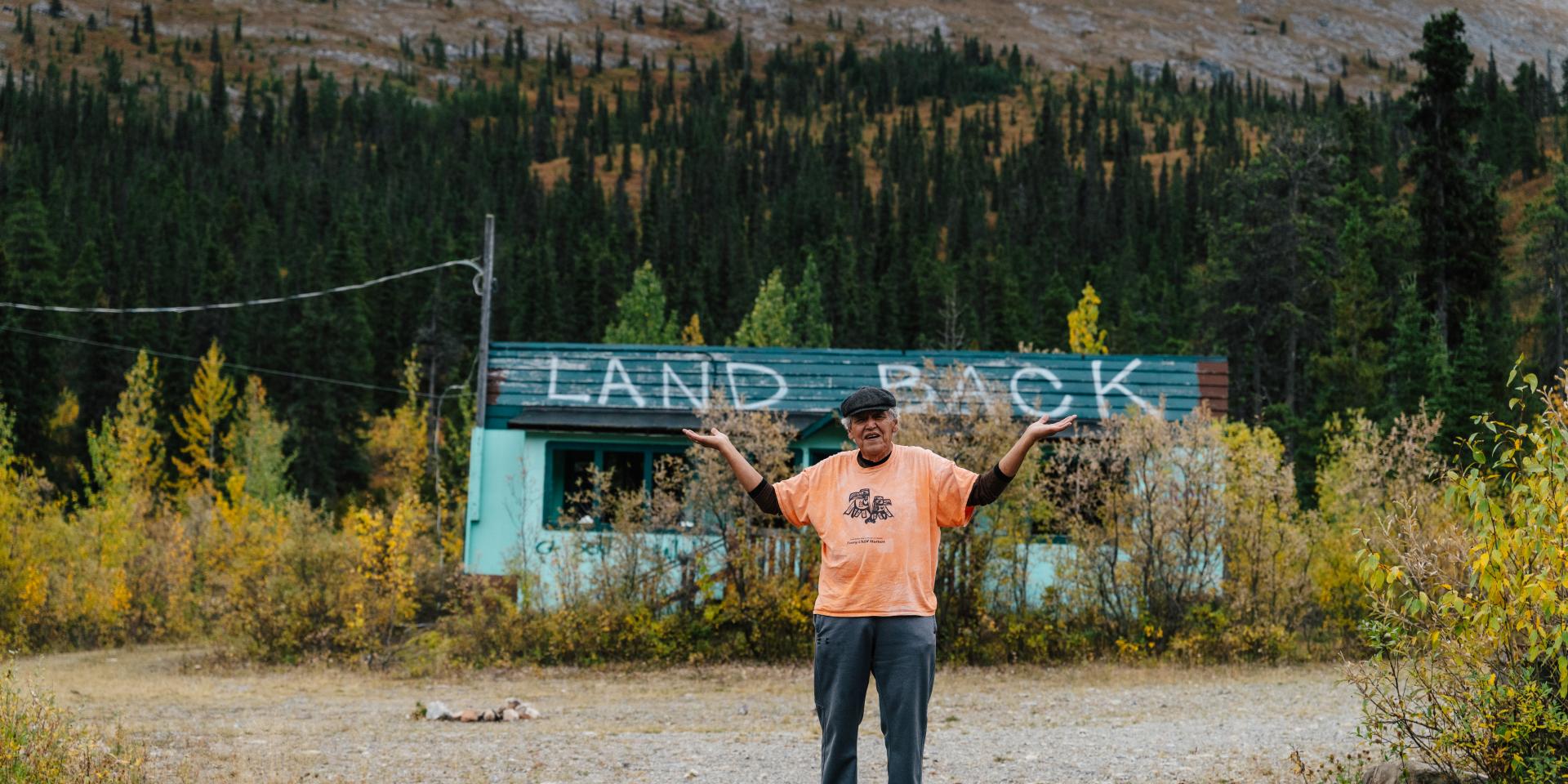 FN member stands before a Land Back sign on the roof of a home in NE B.C.