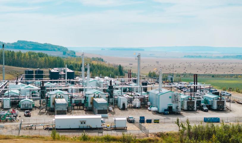 Fracking infrastructure in North Eastern BC against a background of hills, trees and agricultural land
