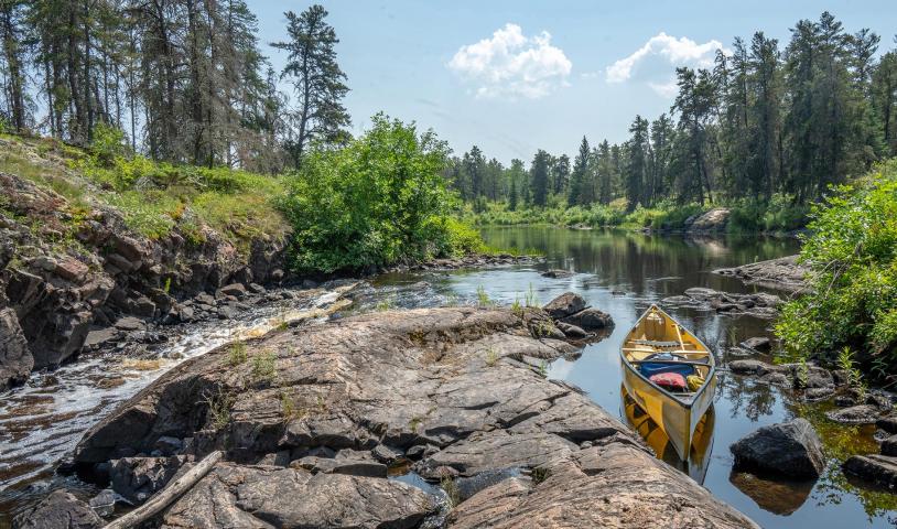 Canoe sitting on rice river, trees and blue sky in the background